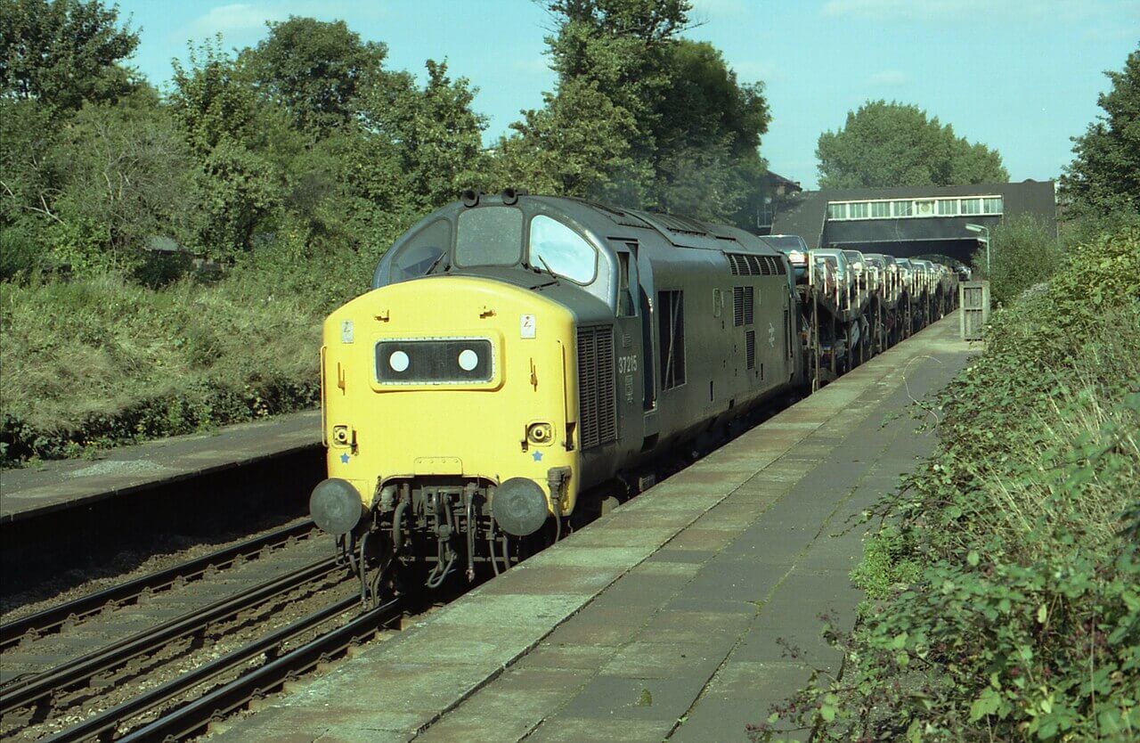 English Electric class 37 diesel locomotive No. 37 215 taking a car carrying train Westwards on a bright sunny day in the 1970s.
